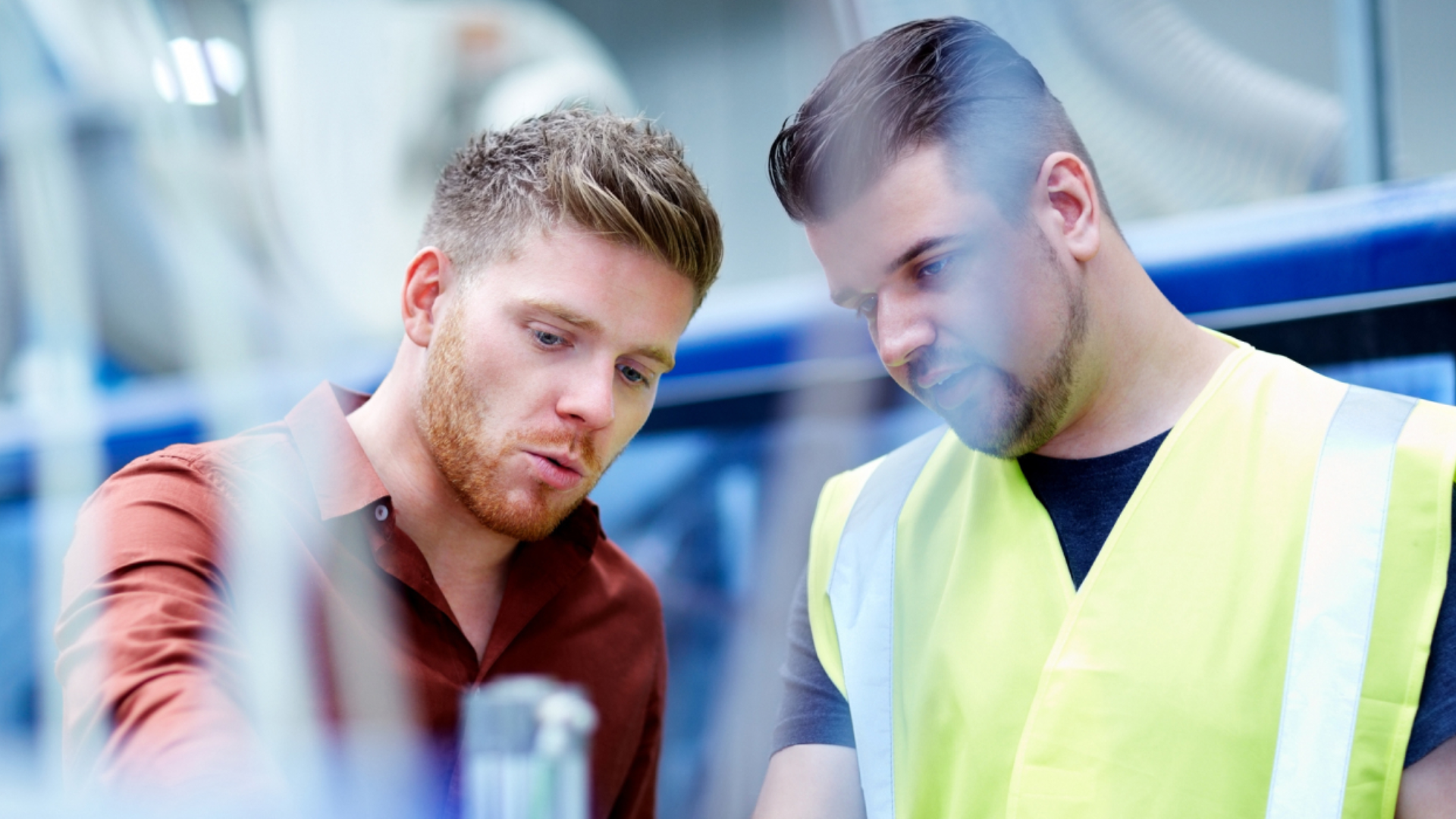 Nærbilde av to menn i samtale – den ene iført rød skjorte, den andre i refleksvest. Foto.