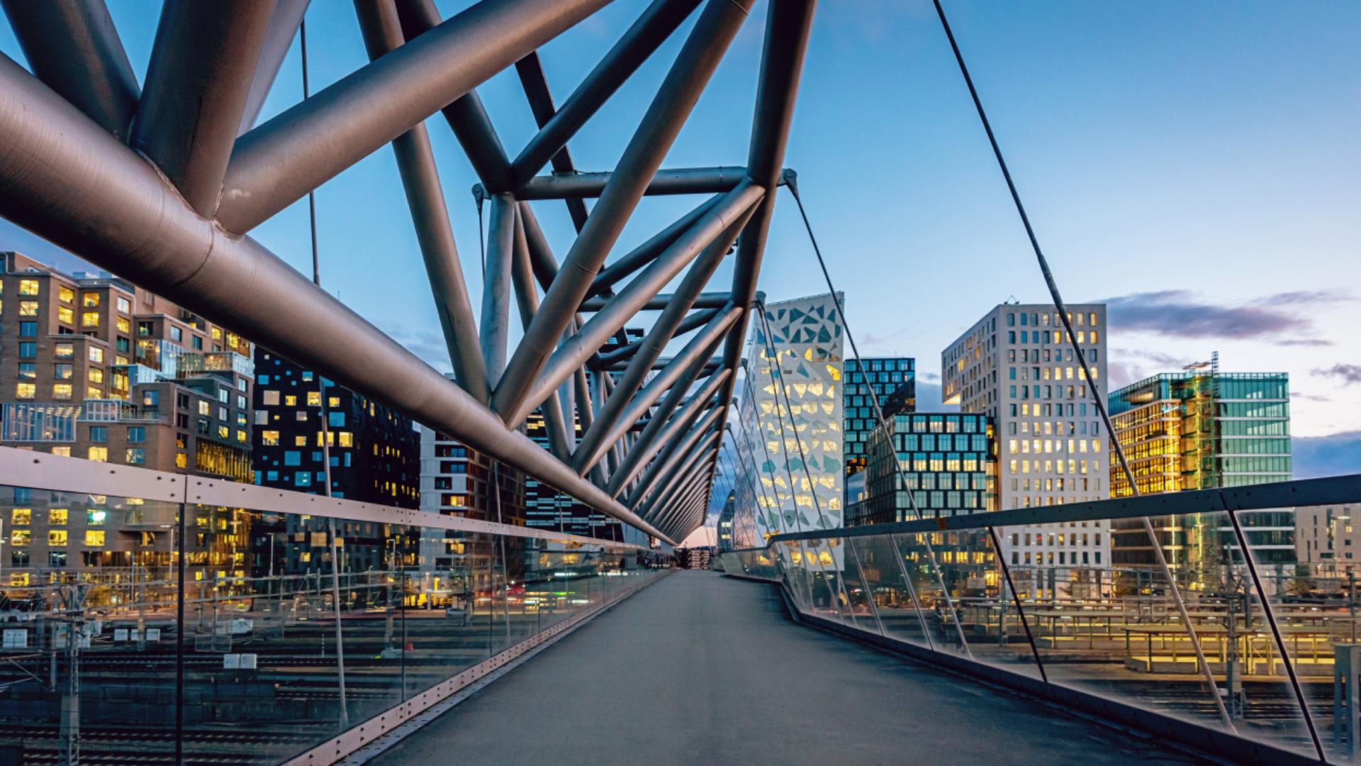 På en moderne bro i forgrunnen ser vi flere bygninger i ulike høyder og farger, med en moderne arkitektonisk stil. Foto.