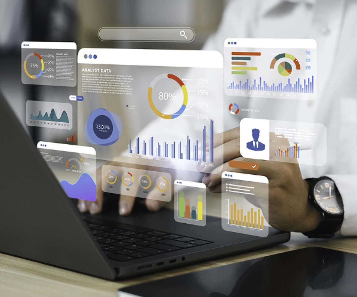 "Nærbilde av baksiden av en laptop, med hender som hviler over tastaturet. Over tastaturet vises små vinduer med dashbordgrafikk og søylediagrammer. Foto og illustrasjon.