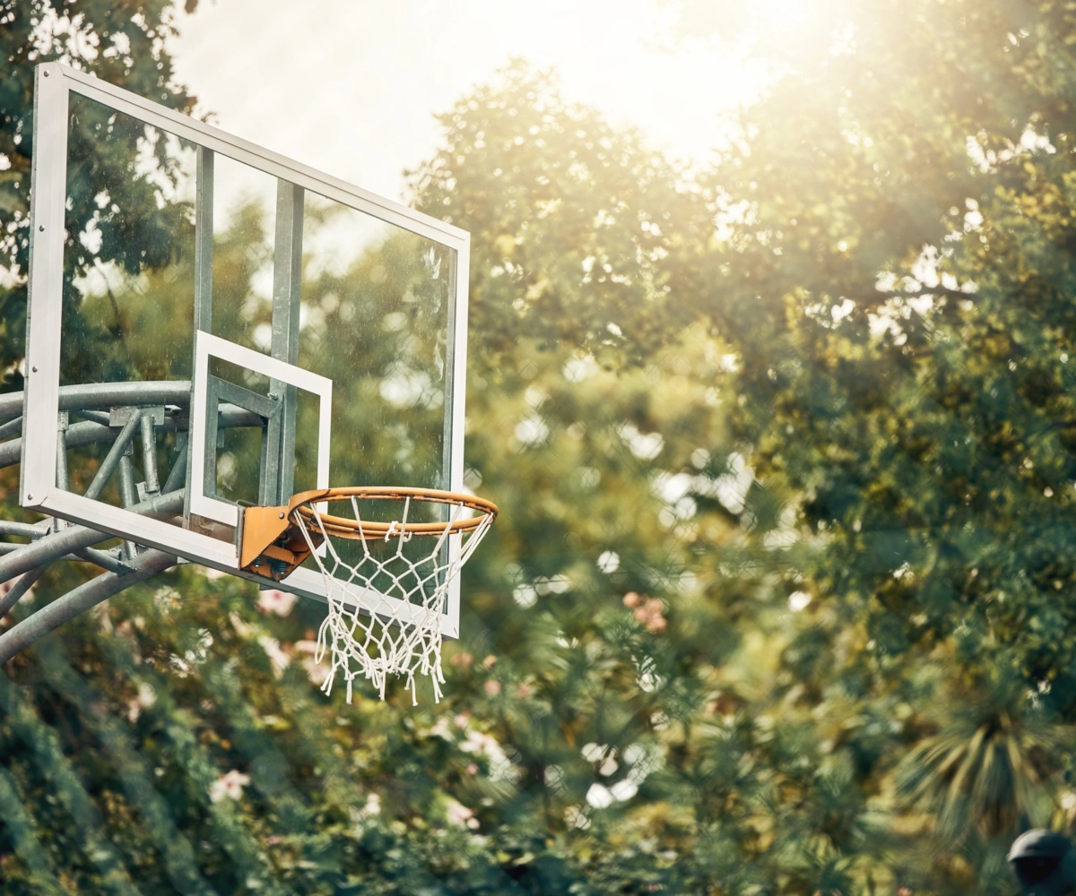Et utendørs basketballstativ omgitt av grønne trær. Foto.