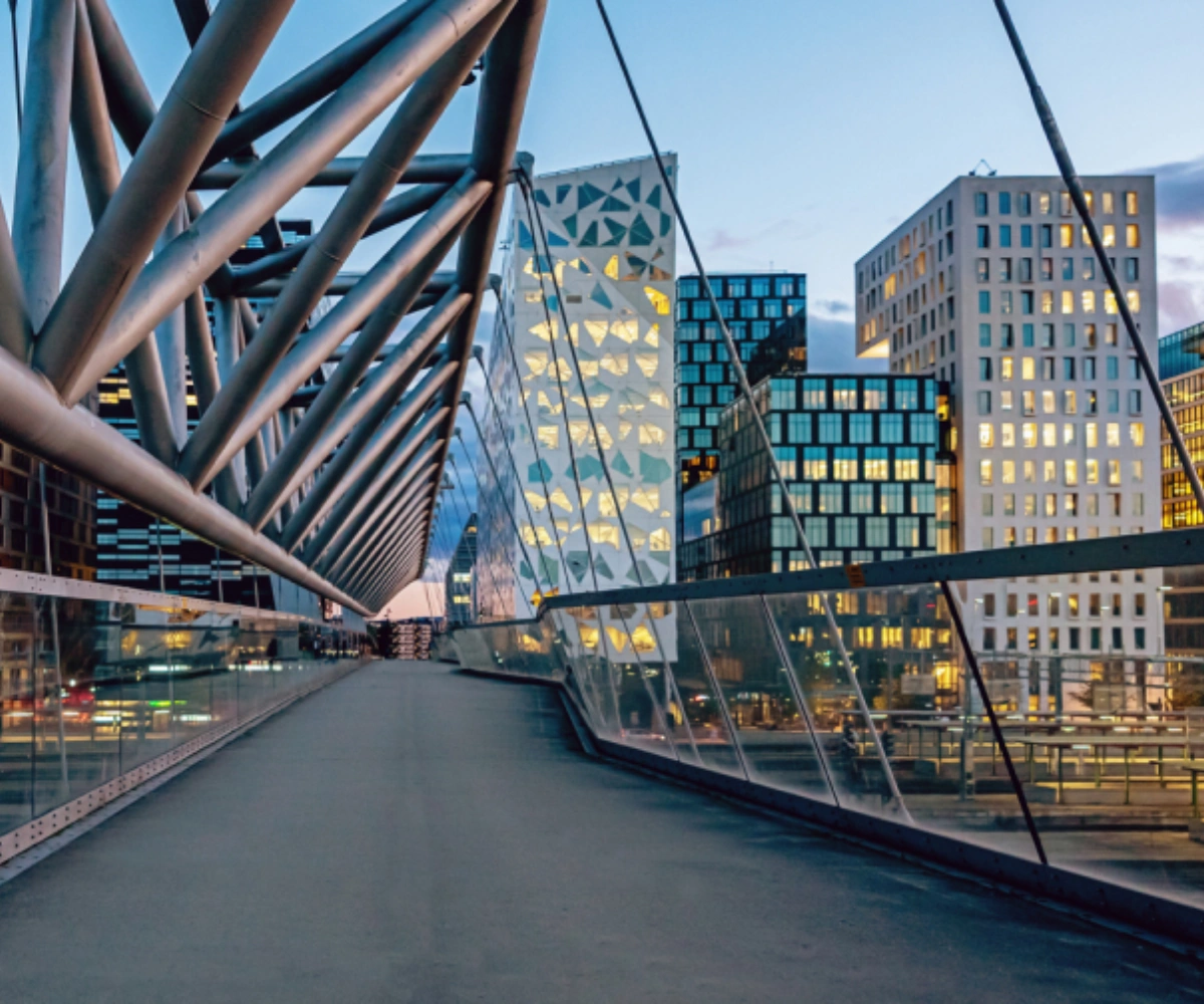 På en moderne bro i forgrunnen ser vi flere bygninger i ulike høyder og farger, med en moderne arkitektonisk stil. Foto.