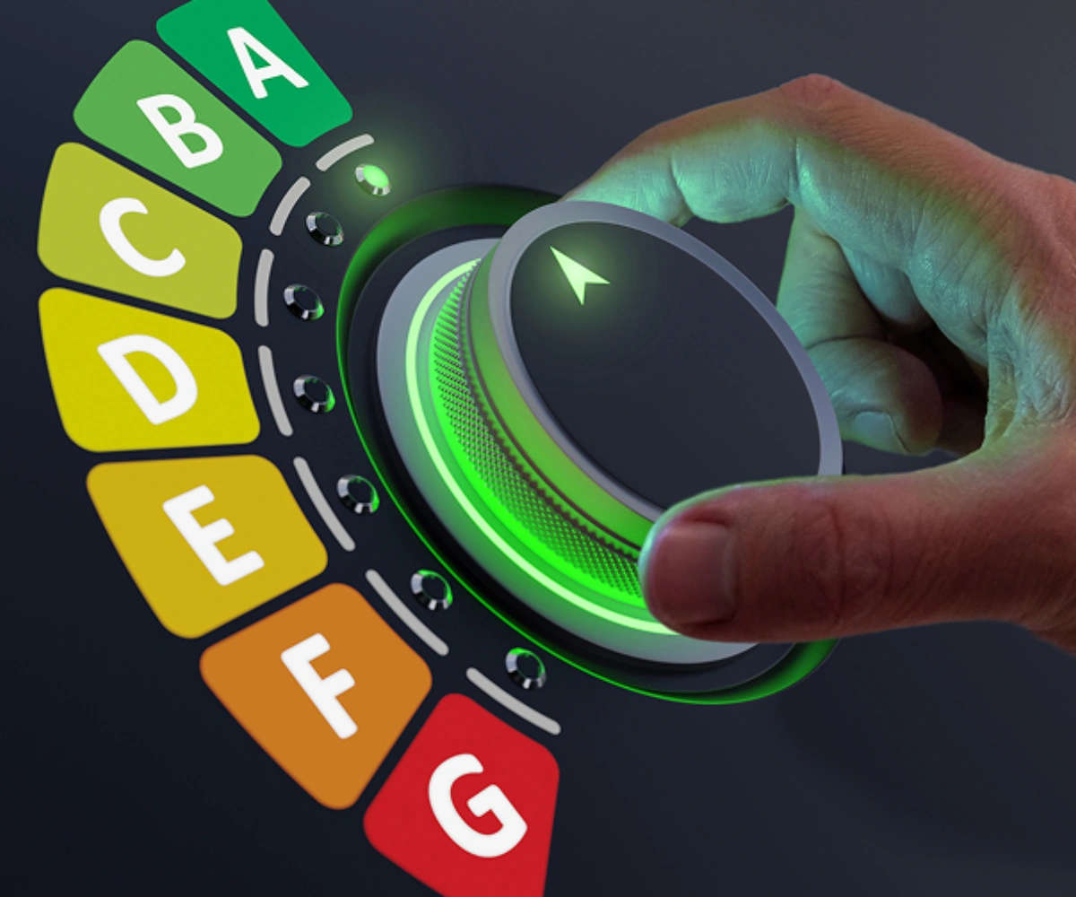 En hånd som styrer en justerbar kontroller, som peker opp mot bokstaven 'A' i grønt. De øvrige bokstavene fra 'A' til 'G' er i en fargepalett som gradvis skifter fra grønn til rød, med nyanser i mellom. Foto.